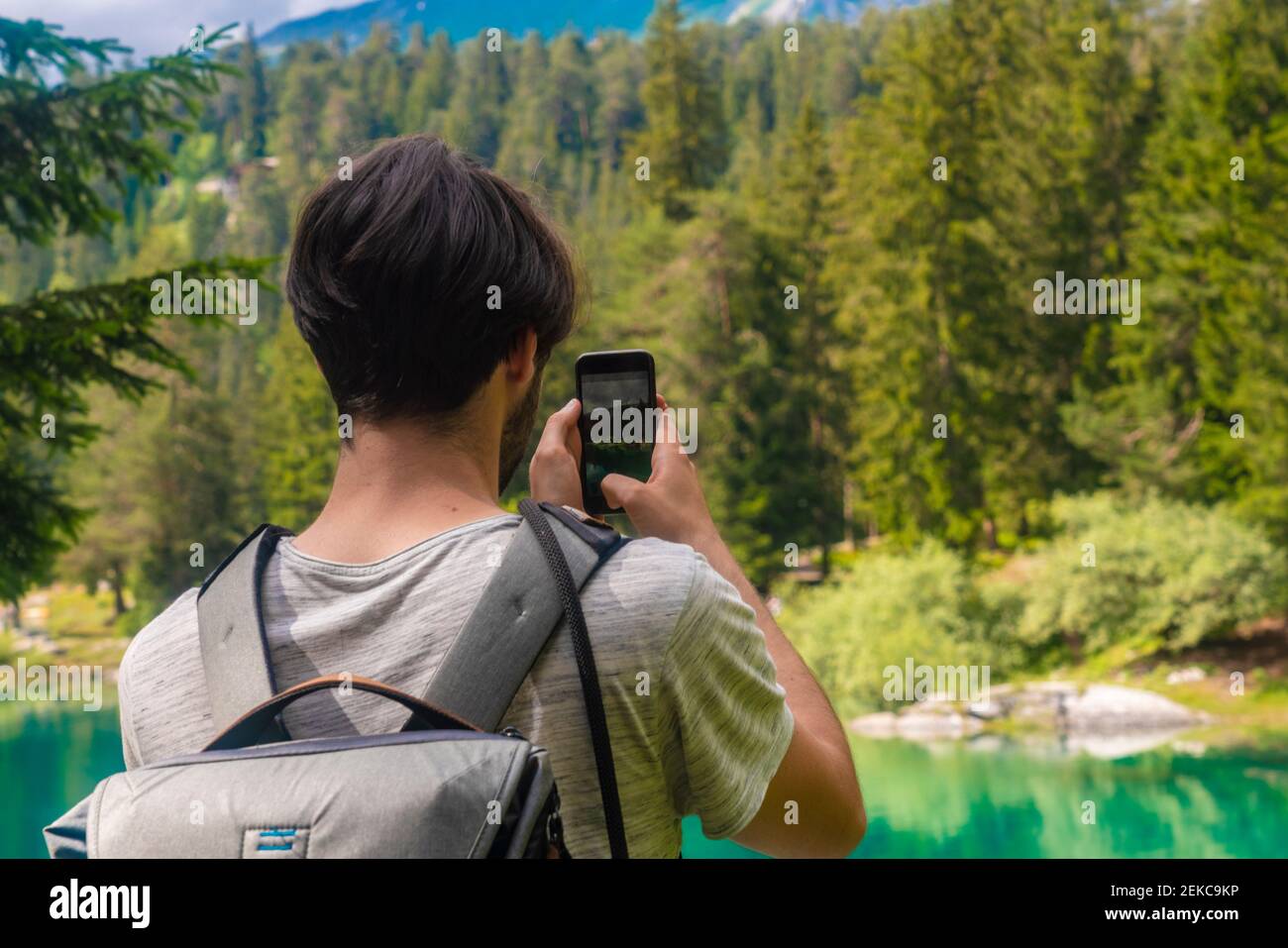 Male hiker taking photo of Cauma Lake through mobile phone while standing at Graubunden Canton, Switzerland Stock Photo