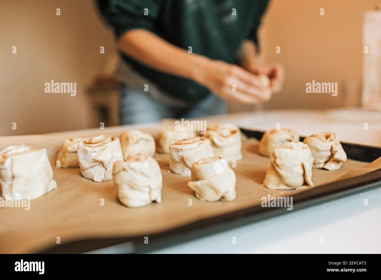 Arranged cinnamon rolls on baking sheet while woman in background at kitchen Stock Photo