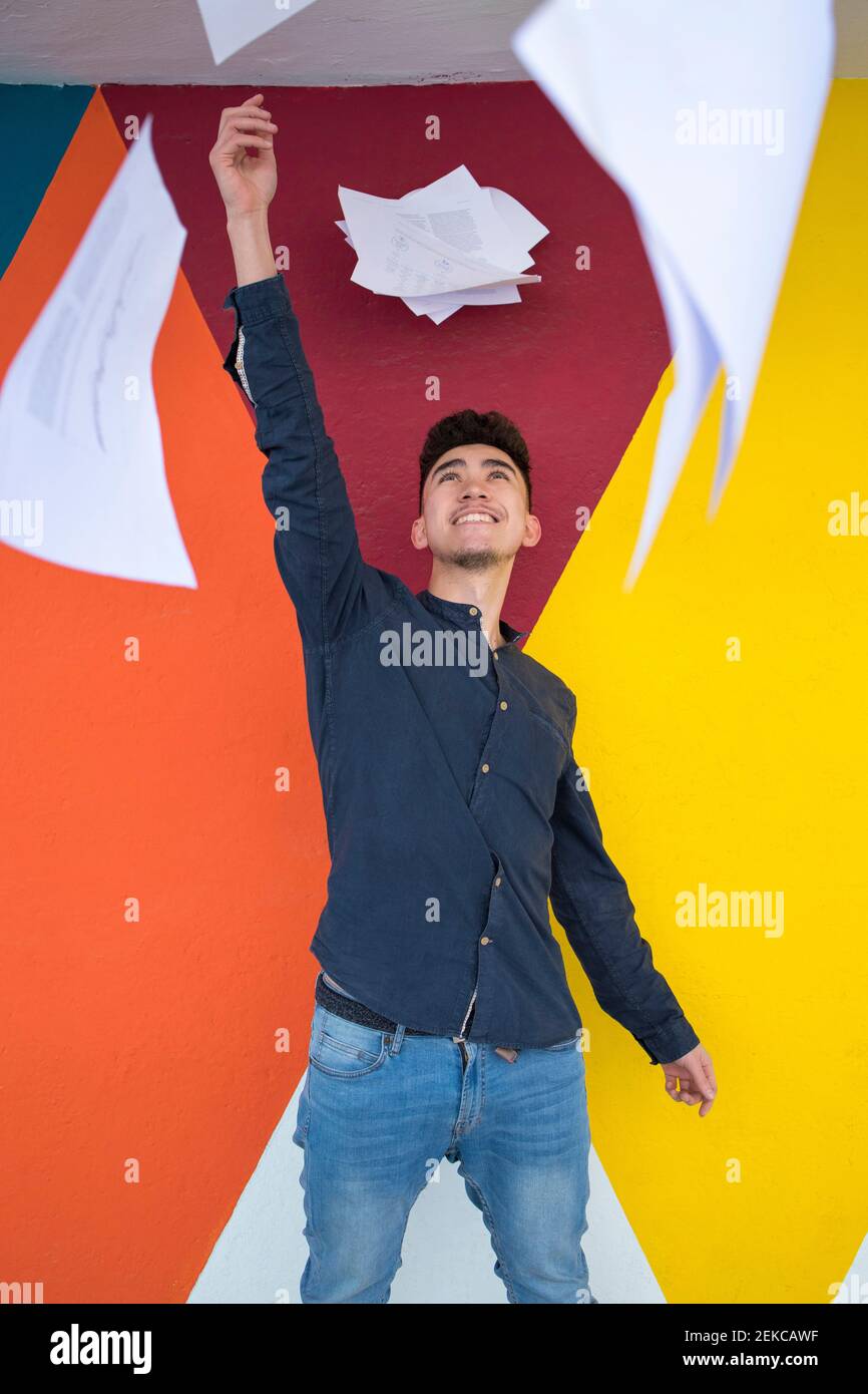 Handsome young man holding bunch of papers against multi colored wall Stock Photo