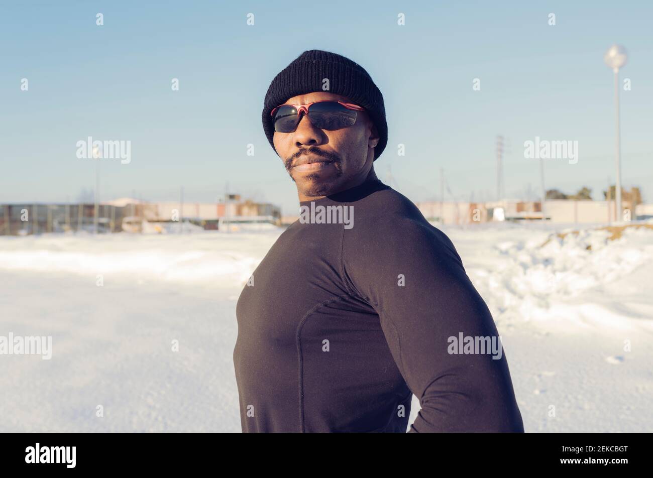 Muscular build sportsman wearing sunglasses standing in snow during sunny day Stock Photo