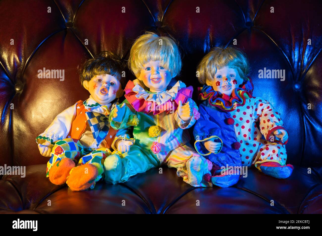 3 colourful porcelain doll children on a red leather sofa Stock Photo