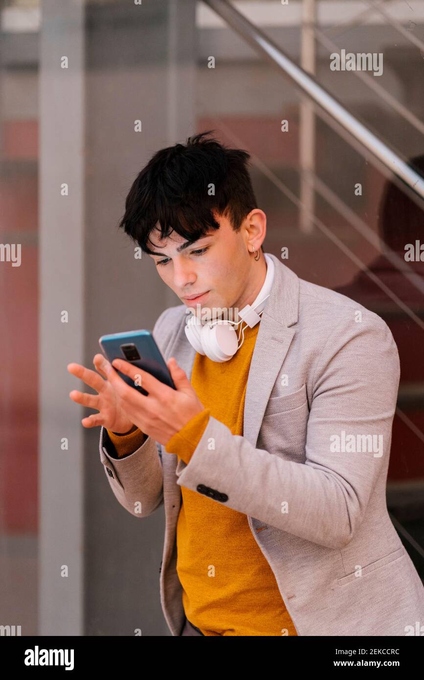 Man with headphones using mobile phone while standing outdoors Stock Photo