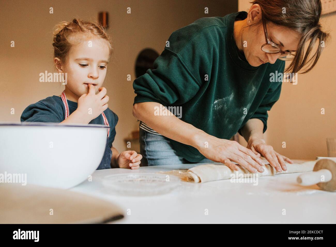 Mother rolling cinnamon roll dough with daughter at home Stock Photo