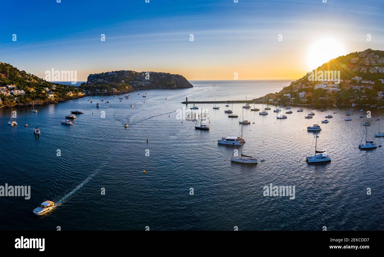 Spain, Balearic Islands, Andratx, Helicopter view of boats sailing near shore of coastal town at sunset Stock Photo