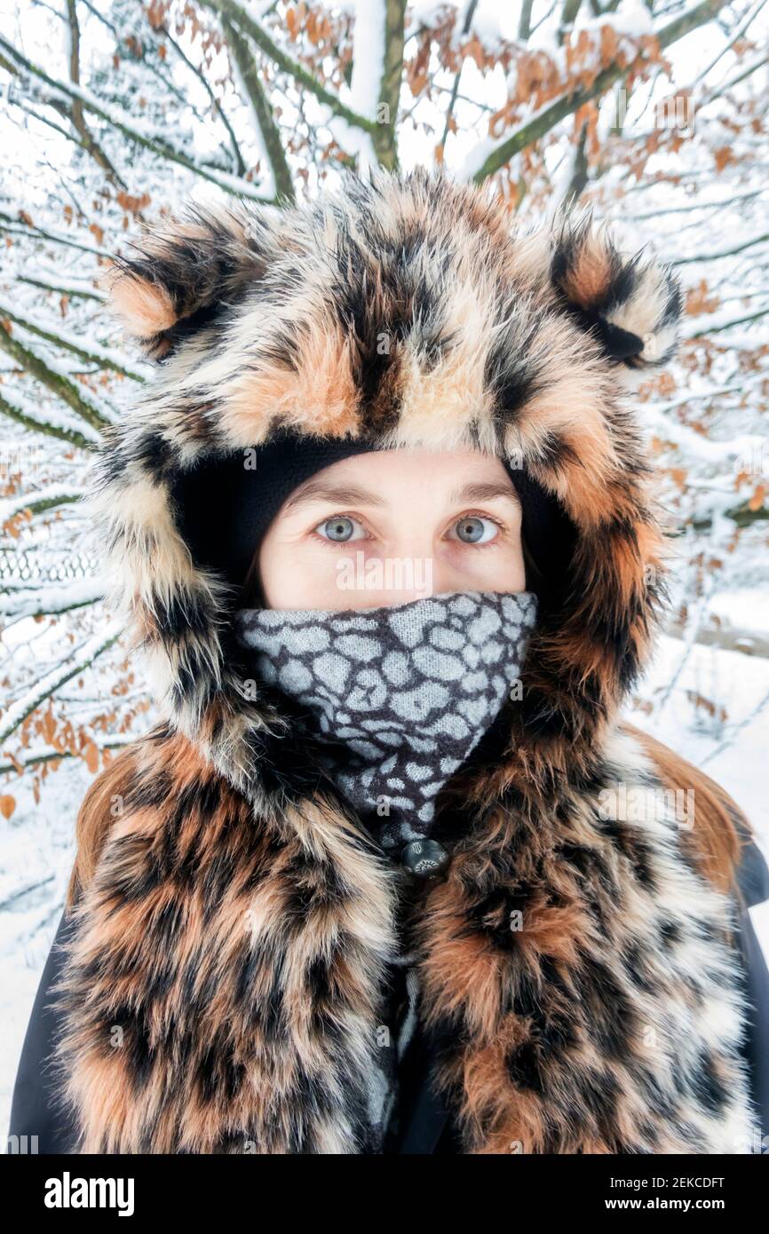 Mature woman wearing leopard print fur hat staring while standing against tree during winter Stock Photo