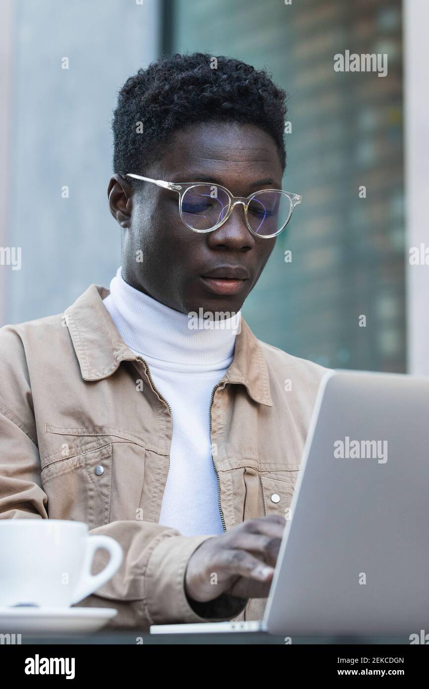 Young man in eyeglasses using laptop at sidewalk cafe Stock Photo