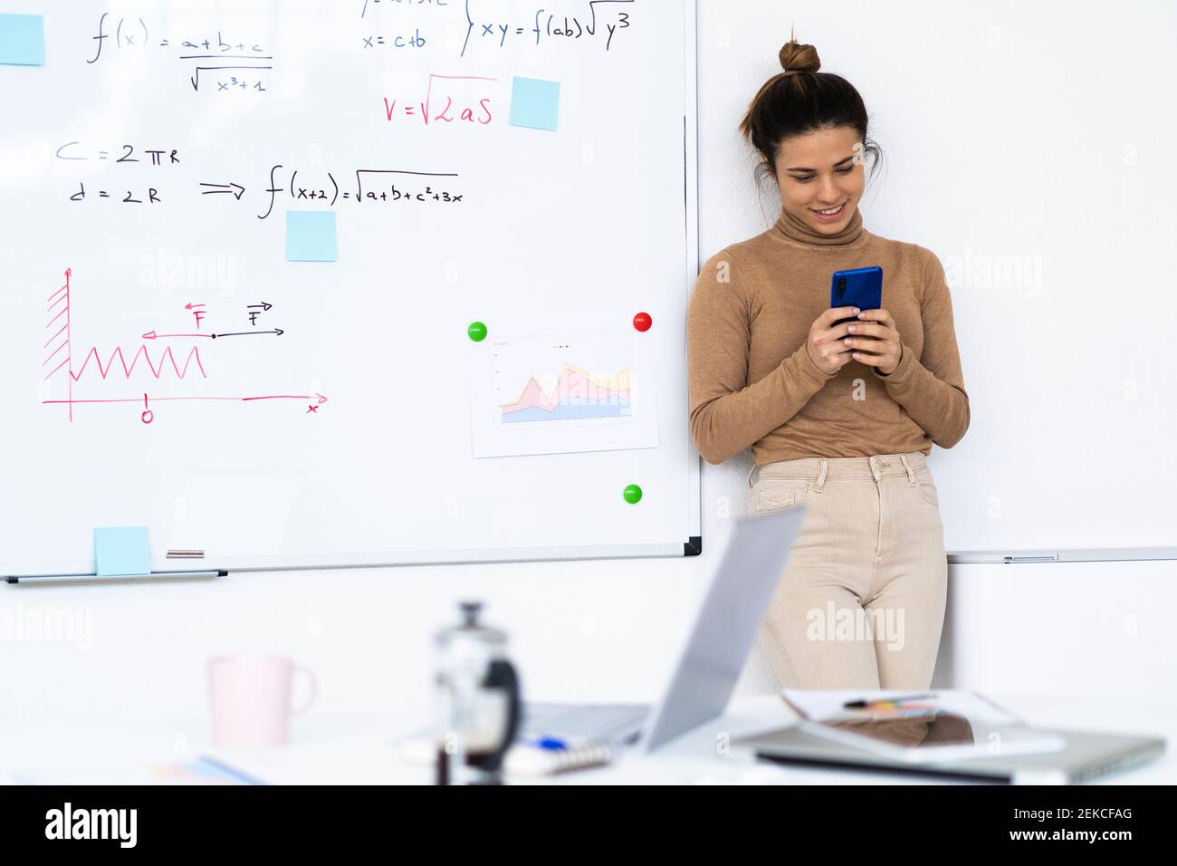 Smiling female student using smartphone while standing against wall Stock Photo