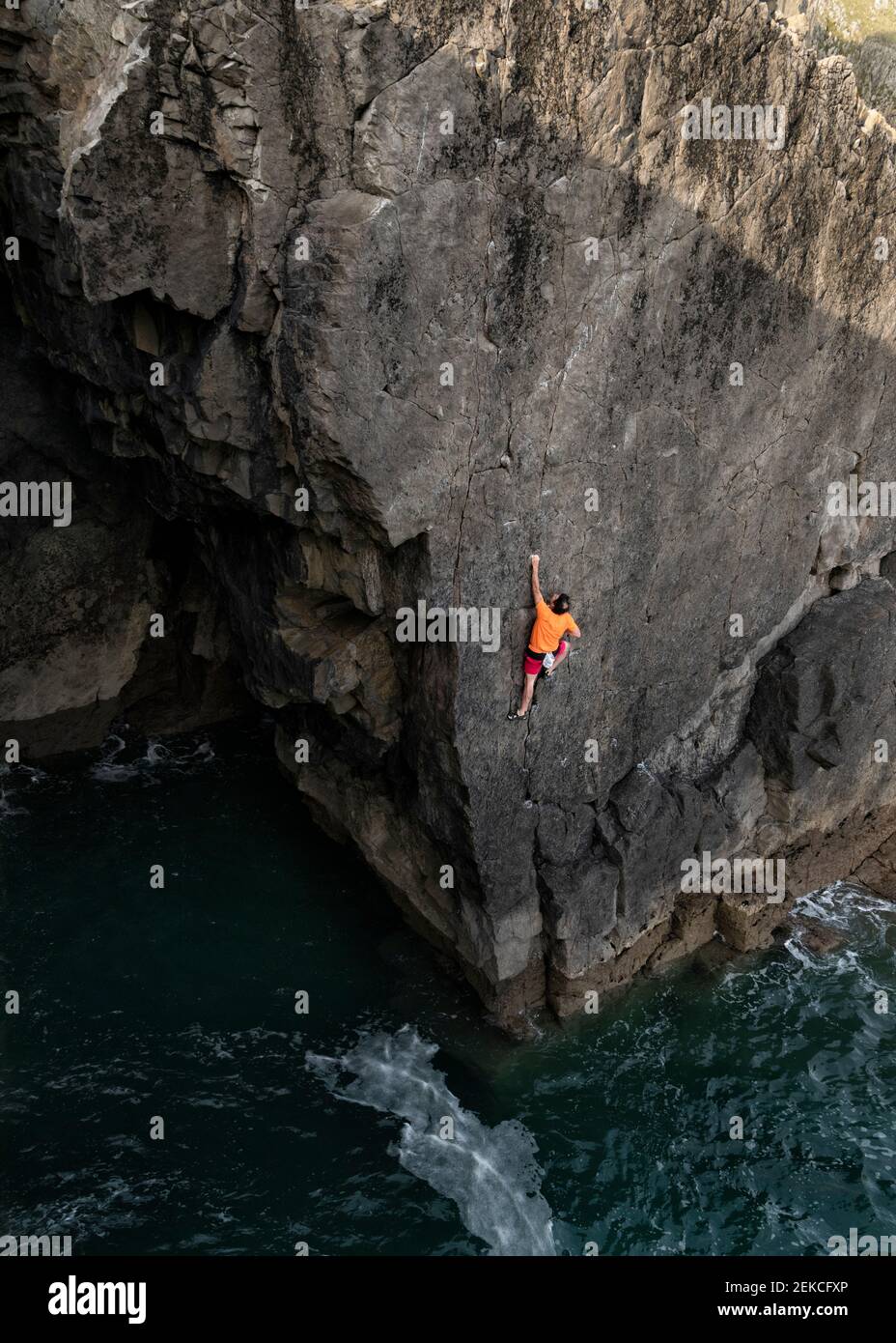 Male rock climber climbing up cliff above water Stock Photo