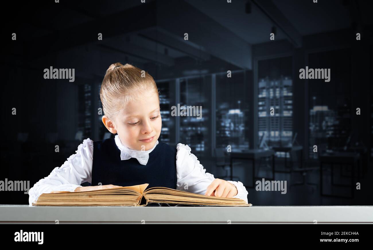 Smiling little girl sitting at desk with open book Stock Photo - Alamy