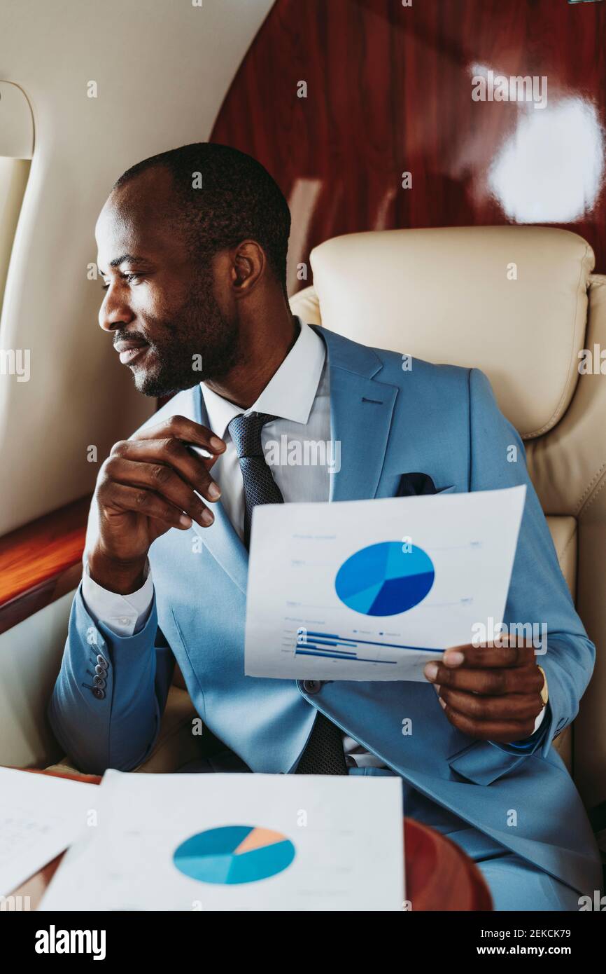 Businessman with pie chart looking through window in airplane Stock Photo