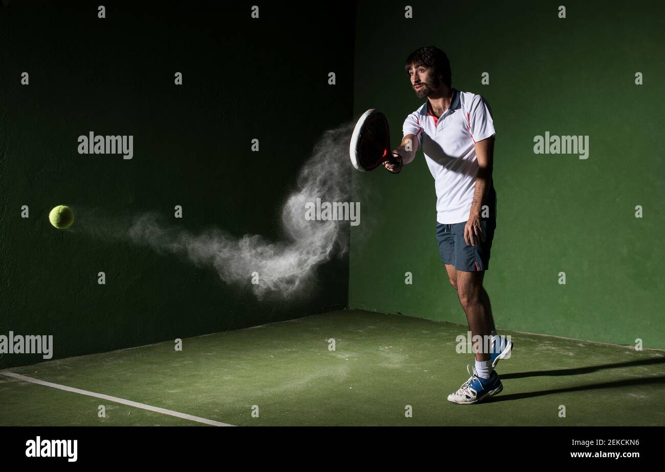 Male athlete servicing ball while playing padel tennis in sports court at night Stock Photo