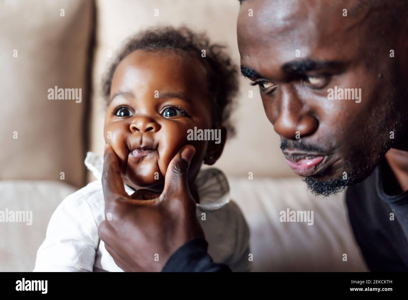 Playful father squeezing baby girl's cheeks at home Stock Photo