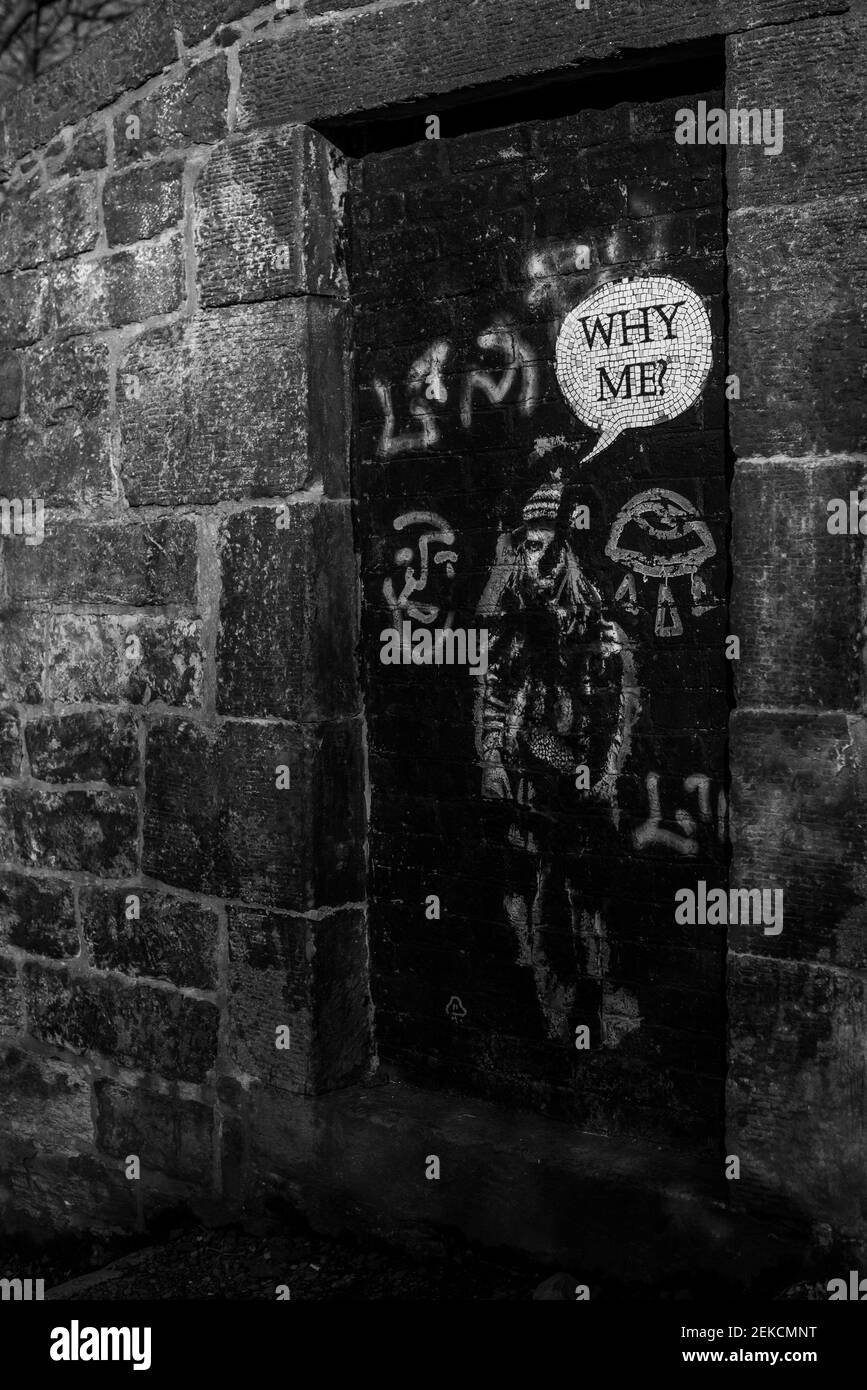 'Why Me' street art girl on door by brick wall on slopes of Calton Hill Edinburgh. Shot in dramatic black and white. Stock Photo
