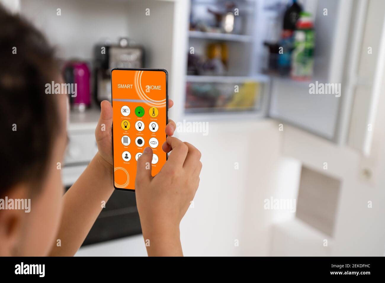little girl holds a smartphone and controls the refrigerator, smart home Stock Photo
