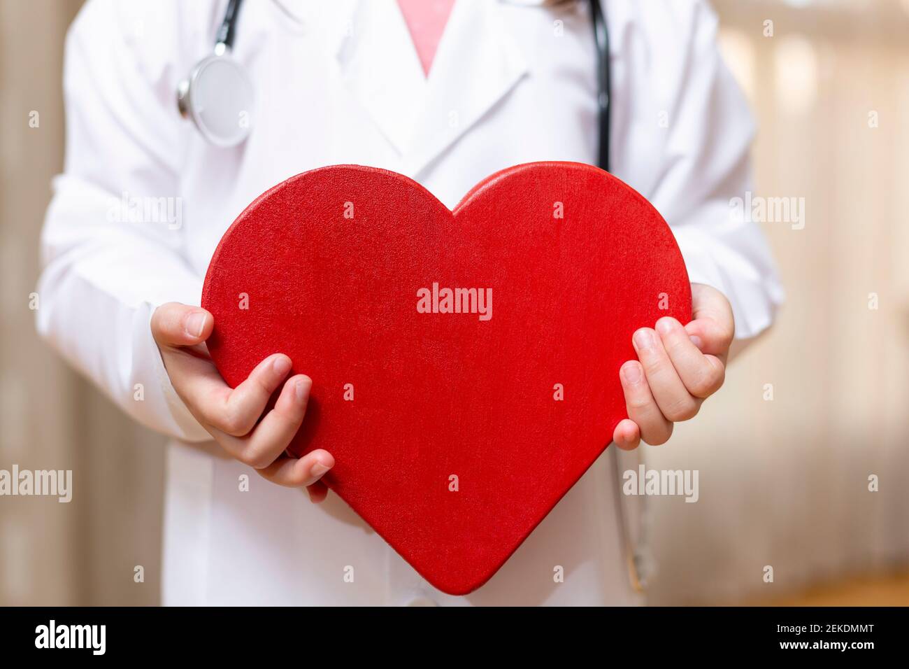 Close up of unrecognizable person in doctor's dress holding a big heart in his hands. Concept of health and wellness. Stock Photo