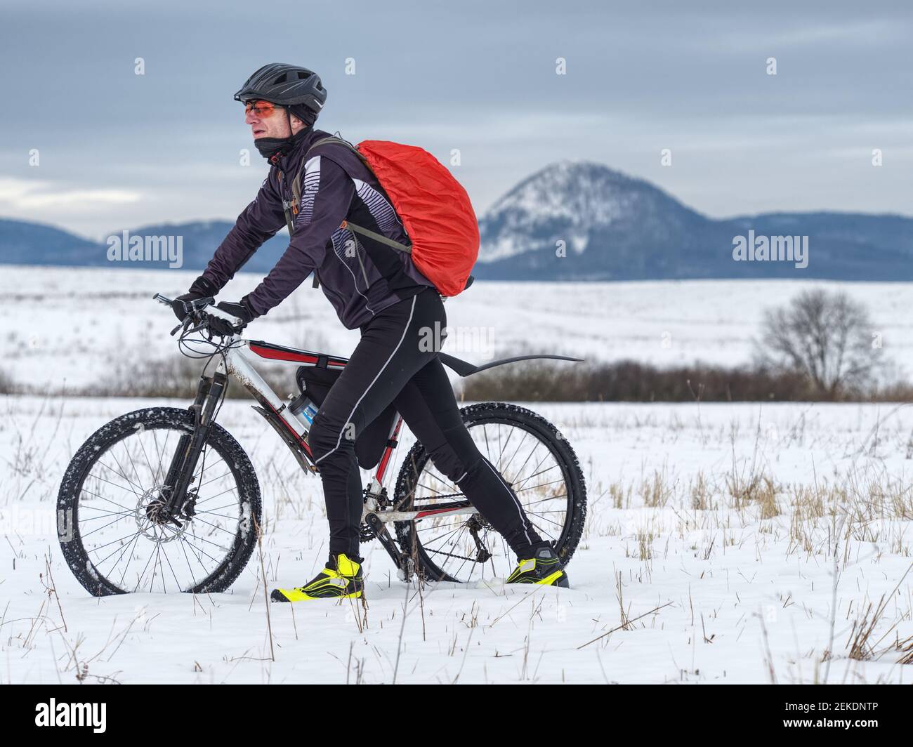 Adult athlete pushes a mountain bike through the snow across a frozen