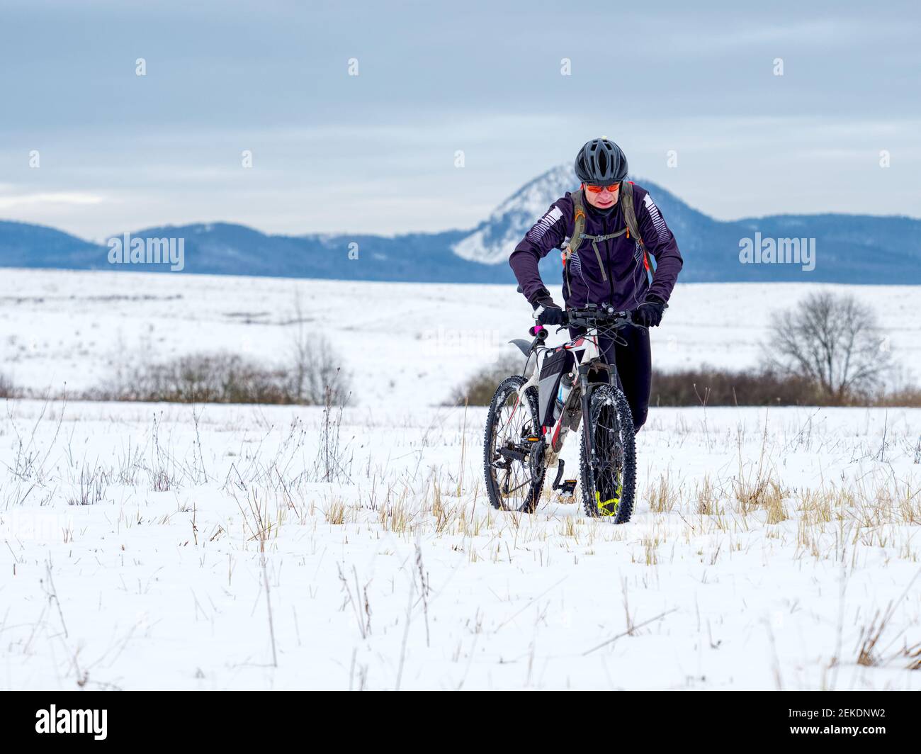 Adult athlete pushes a mountain bike through the snow across a frozen