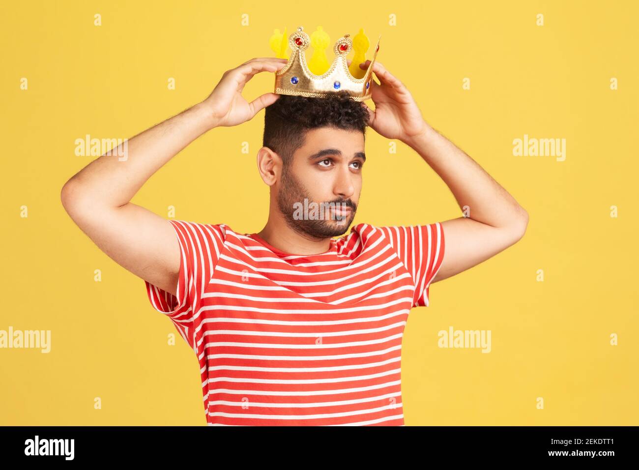 Ambitious bearded man wearing golden crown, imagining promotion at work to position of top manager or boss, looking with arrogance, privileged status. Stock Photo