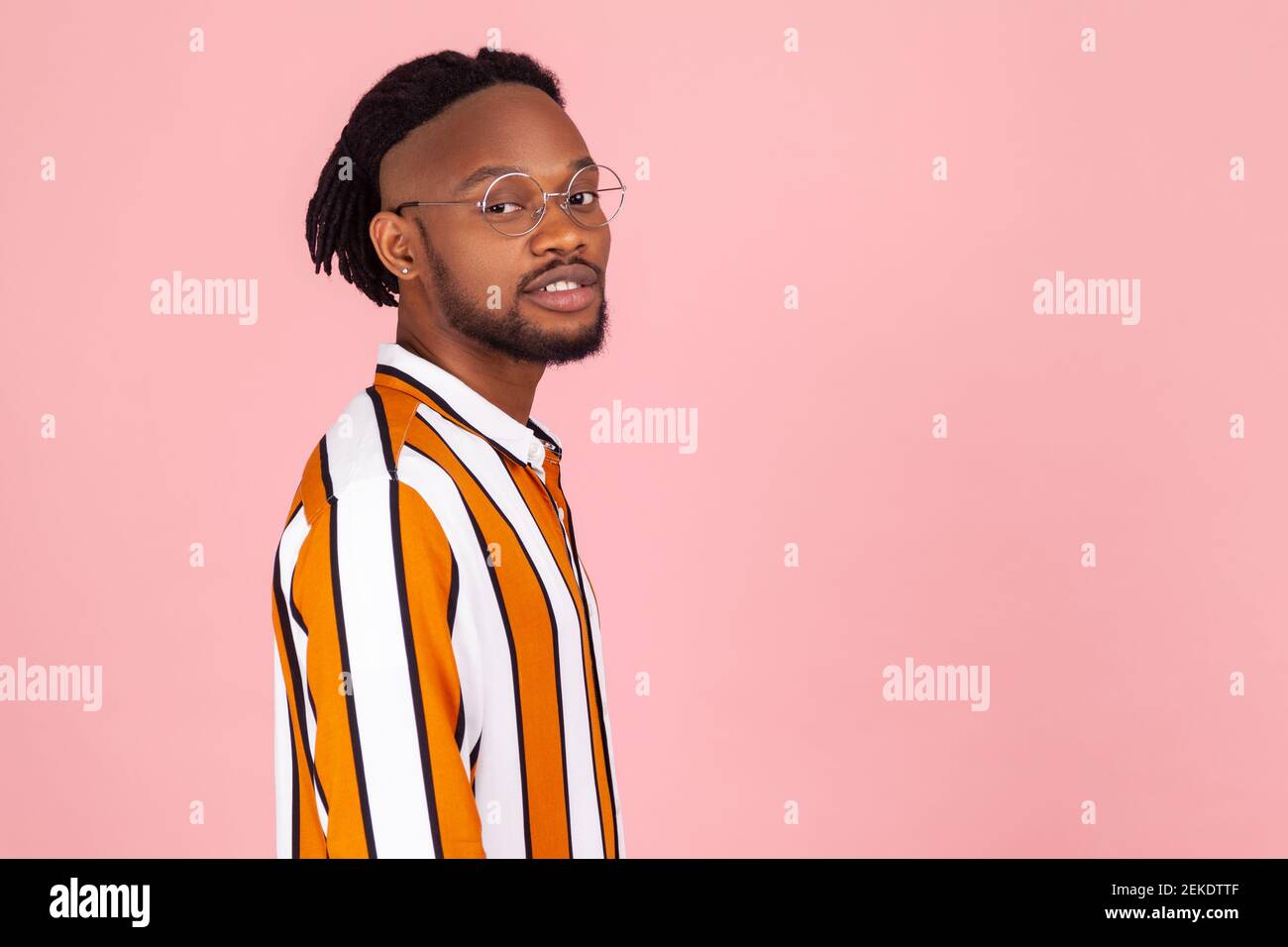 Half turn portrait stylish african man with dreadlocks and ear piercing in striped shirt looking at camera with calm confident expression. Indoor stud Stock Photo