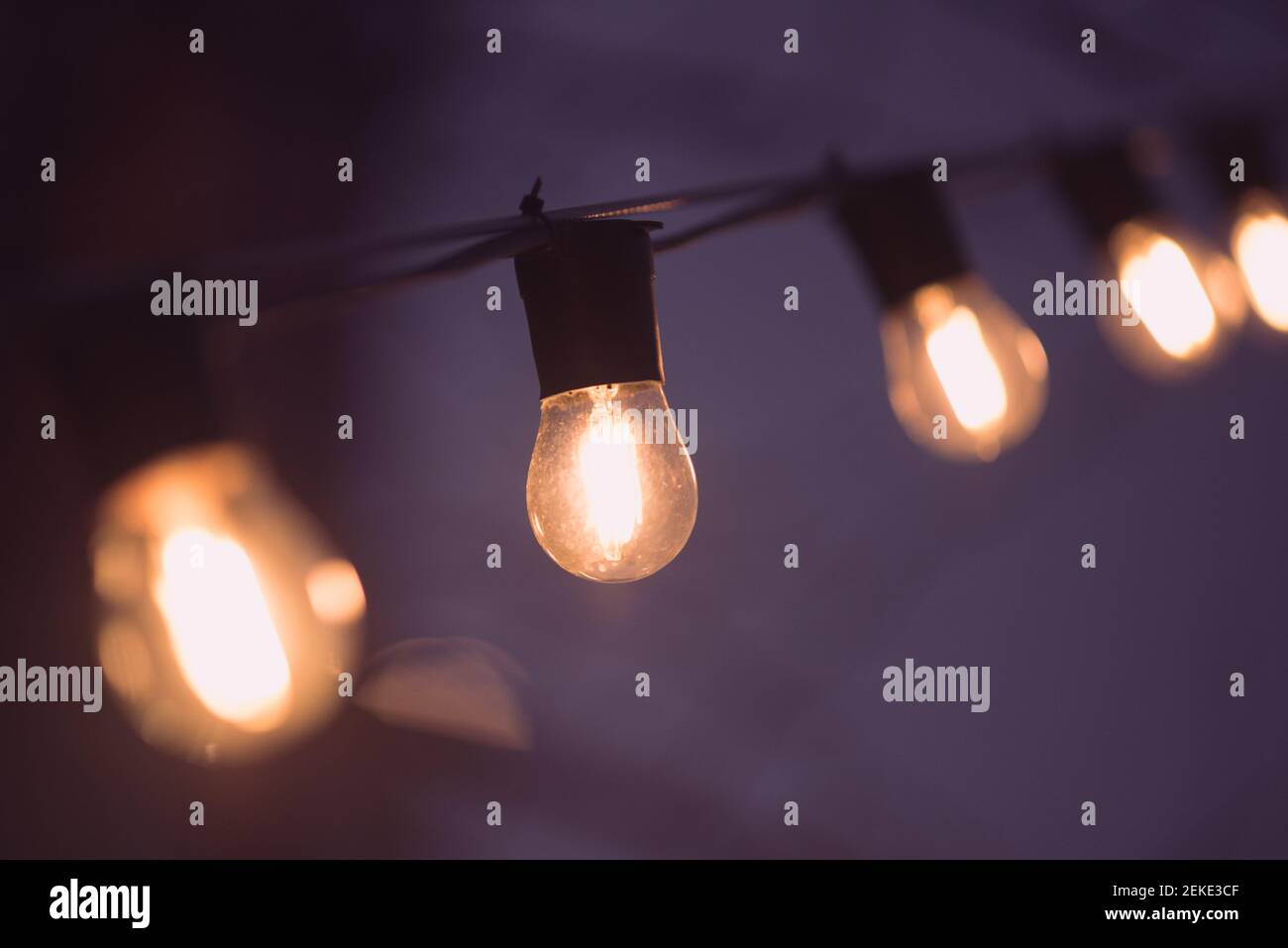 Garland of bulb lamps in darkness. Warm orange light in purple night. Stock Photo