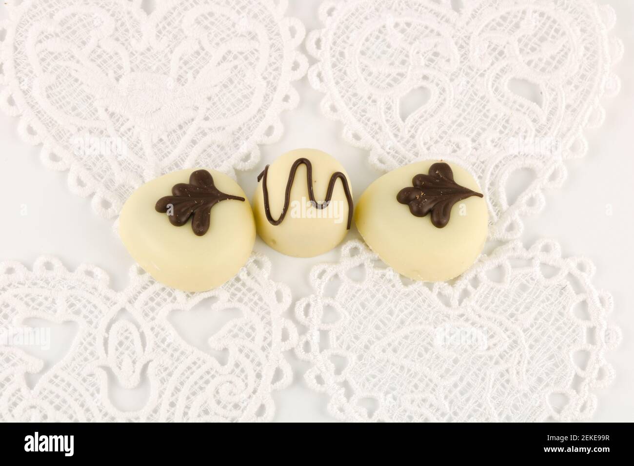 Three luxury chocolates on white hearts with copy space, sheer indulgence concept Stock Photo