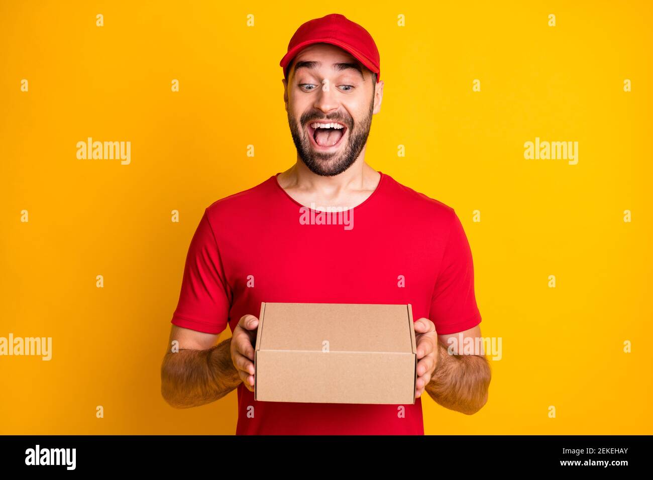 Photo portrait of funny laughing man delivering carton package in red clothes isolated on vivid yellow color background Stock Photo