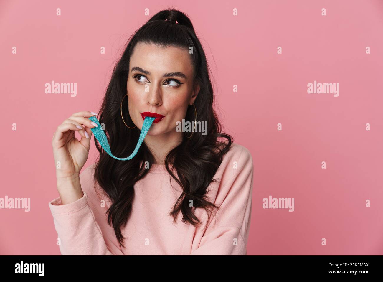 Serious beautiful girl looking aside eating chewing marmalade isolated