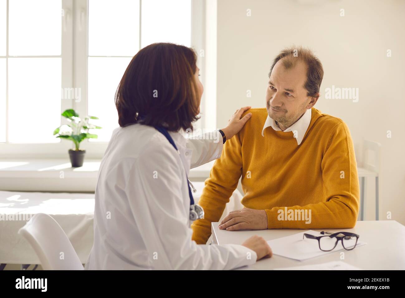 Doctor touches patient's shoulder to support and reassure him during visit to clinic Stock Photo