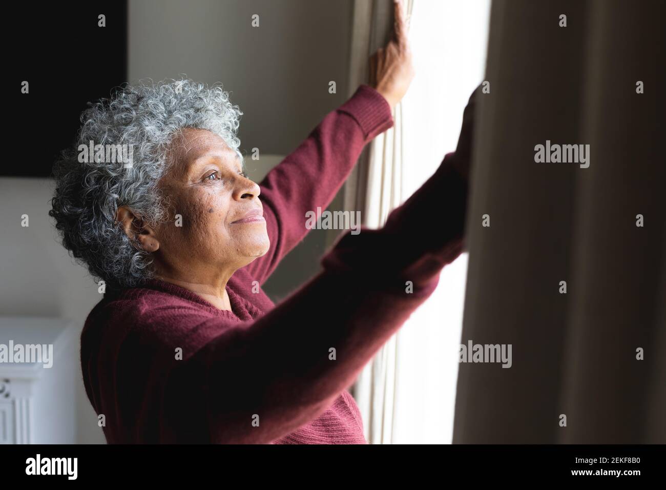 Thoughtful african american senior woman opening window curtains at home Stock Photo