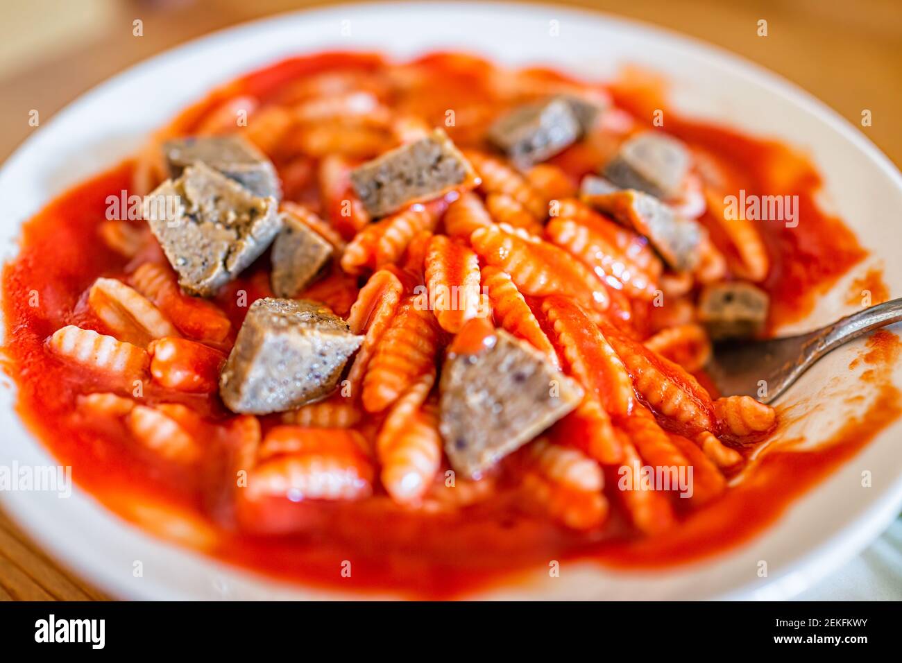 Closeup of bowl with vegan sausage pieces and pasta gnocchi sardi Sardinian shape with red tomato marinara sauce with fork or spoon Stock Photo