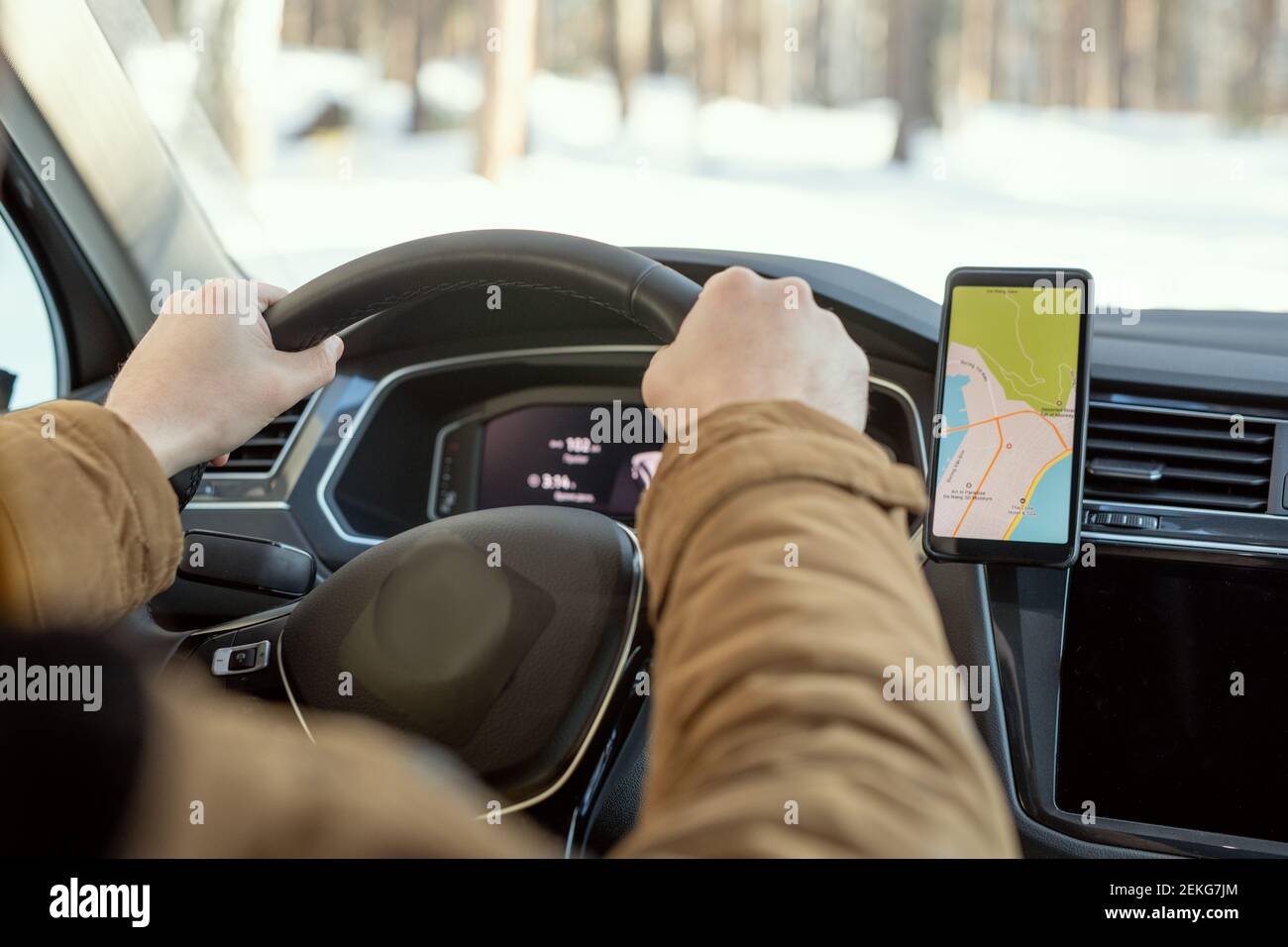 Hands of young contemporary active man in warm winterwear holding by steer while sitting in car and using map on screen of smartphone Stock Photo