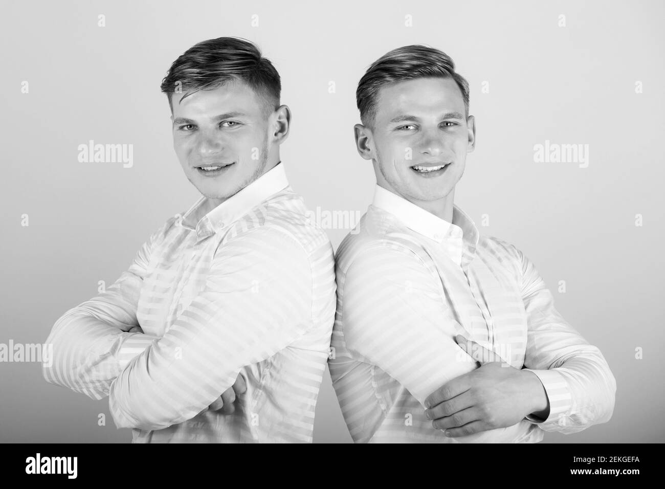 Two brothers smiling. Happy men with hands folded. Models gays standing together. Twins wearing shirts. Family, brotherhood and friendship concept. Stock Photo