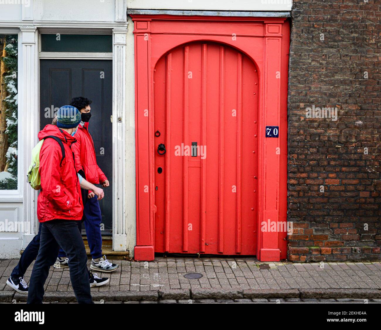 Cambridge , UK, 20-02-2021., Three adults walking in street past ornate red door. Stock Photo