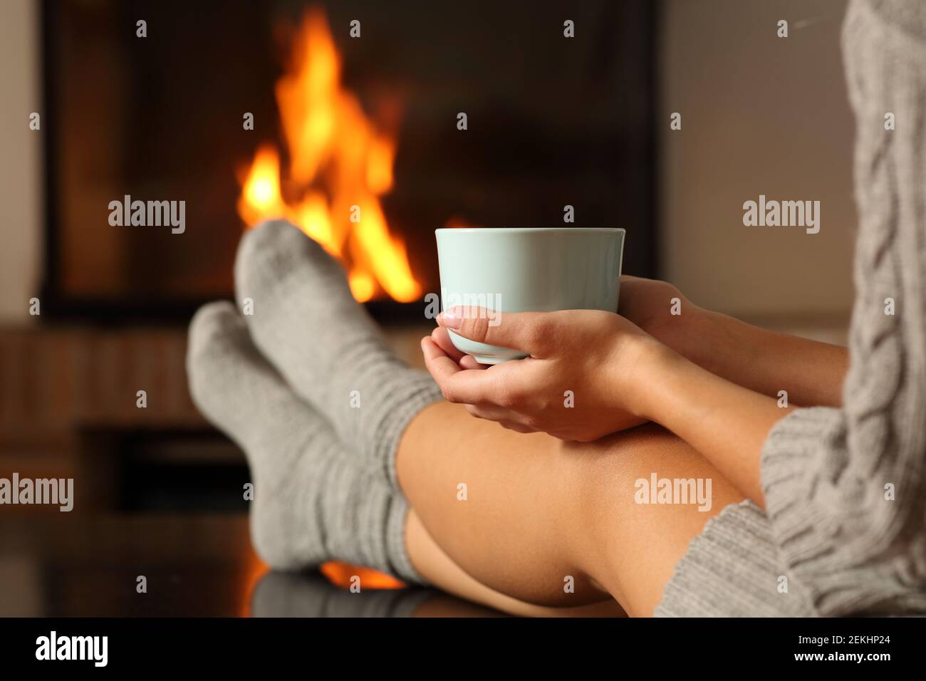 Close up of a woman with socks holding coffee cup in front a fireplace at home in winter Stock Photo