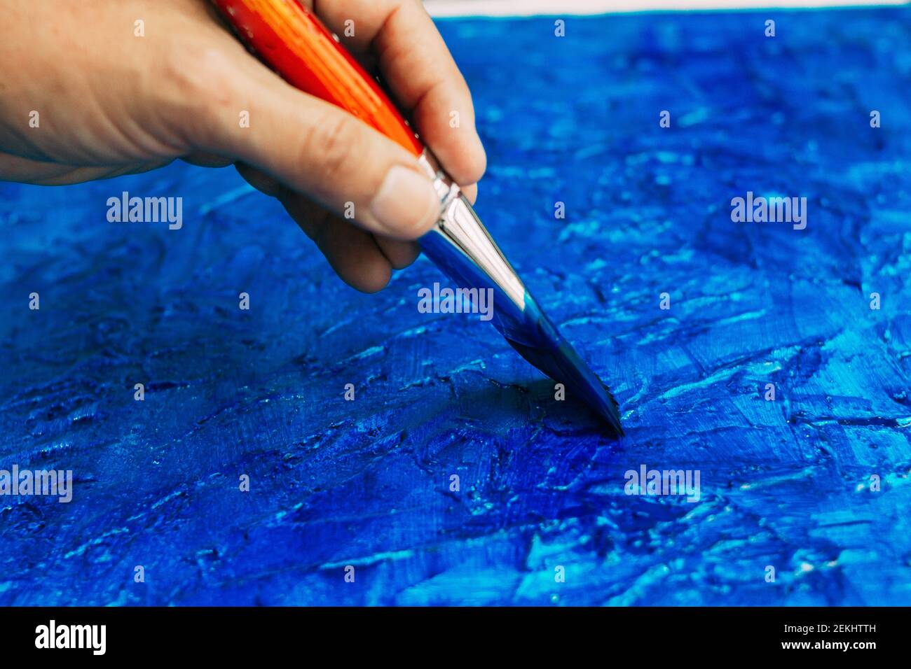 Selective focus of a hand with an artist brush painting a textured blue picture Stock Photo