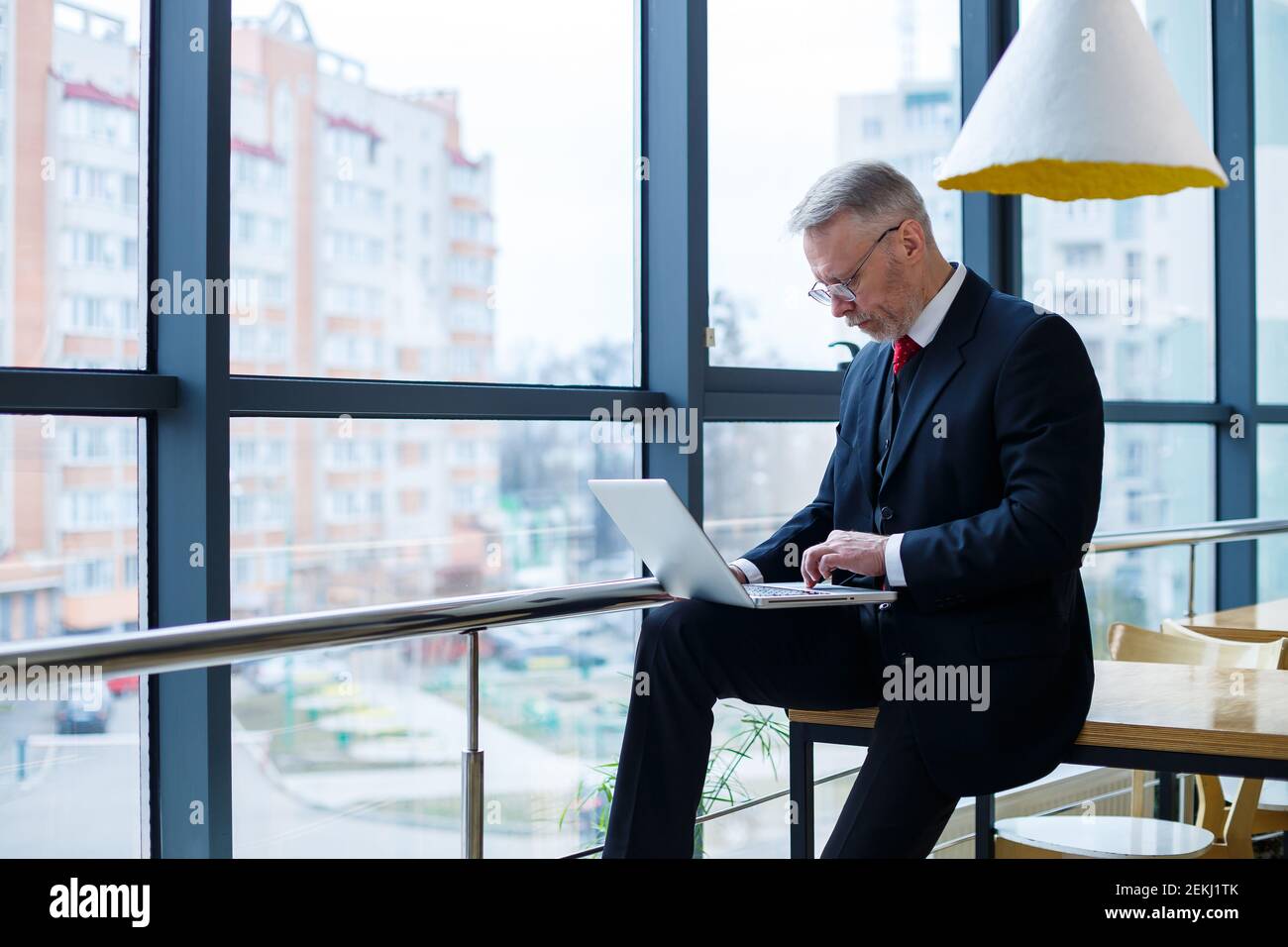 Smiling happy managing director thinks about his successful career development while standing with a laptop in his office near the background of a win Stock Photo