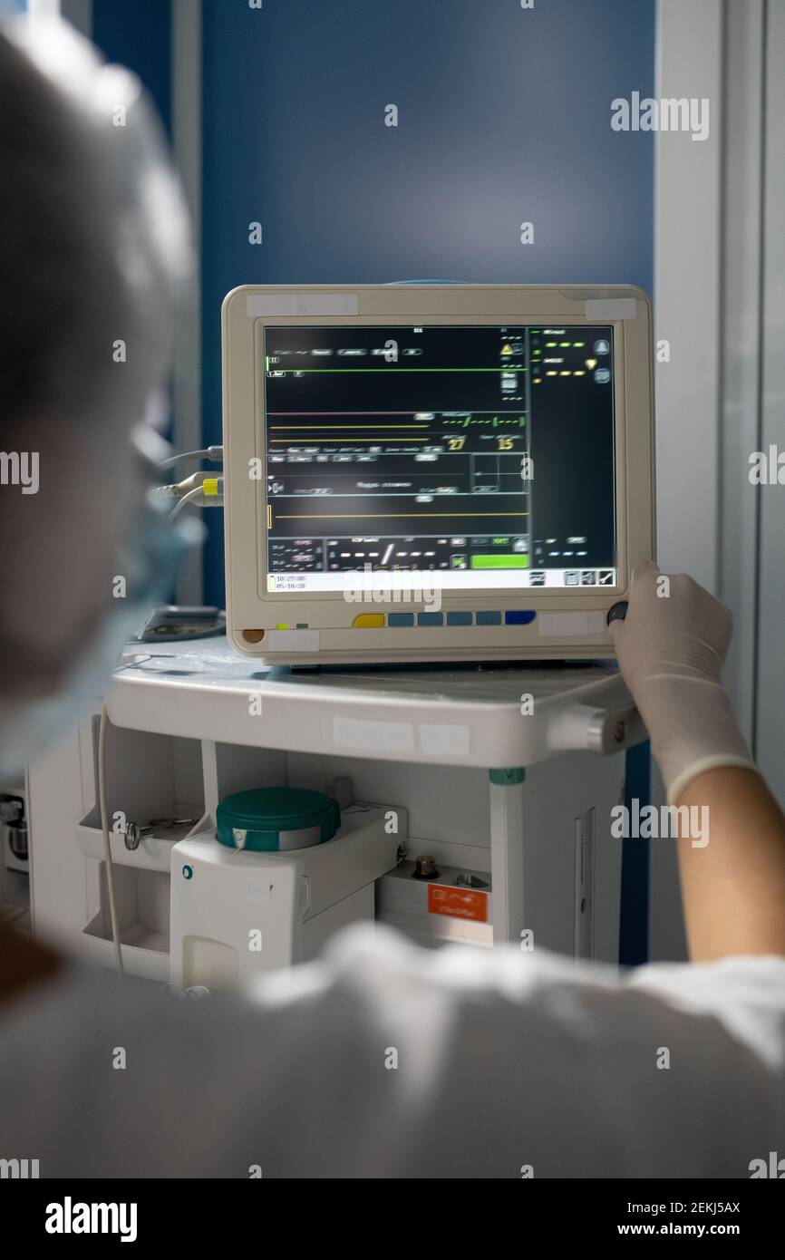 Gloved hand of young female assistant of surgeon standing in front of medical equipment while taking control of patient body condition Stock Photo