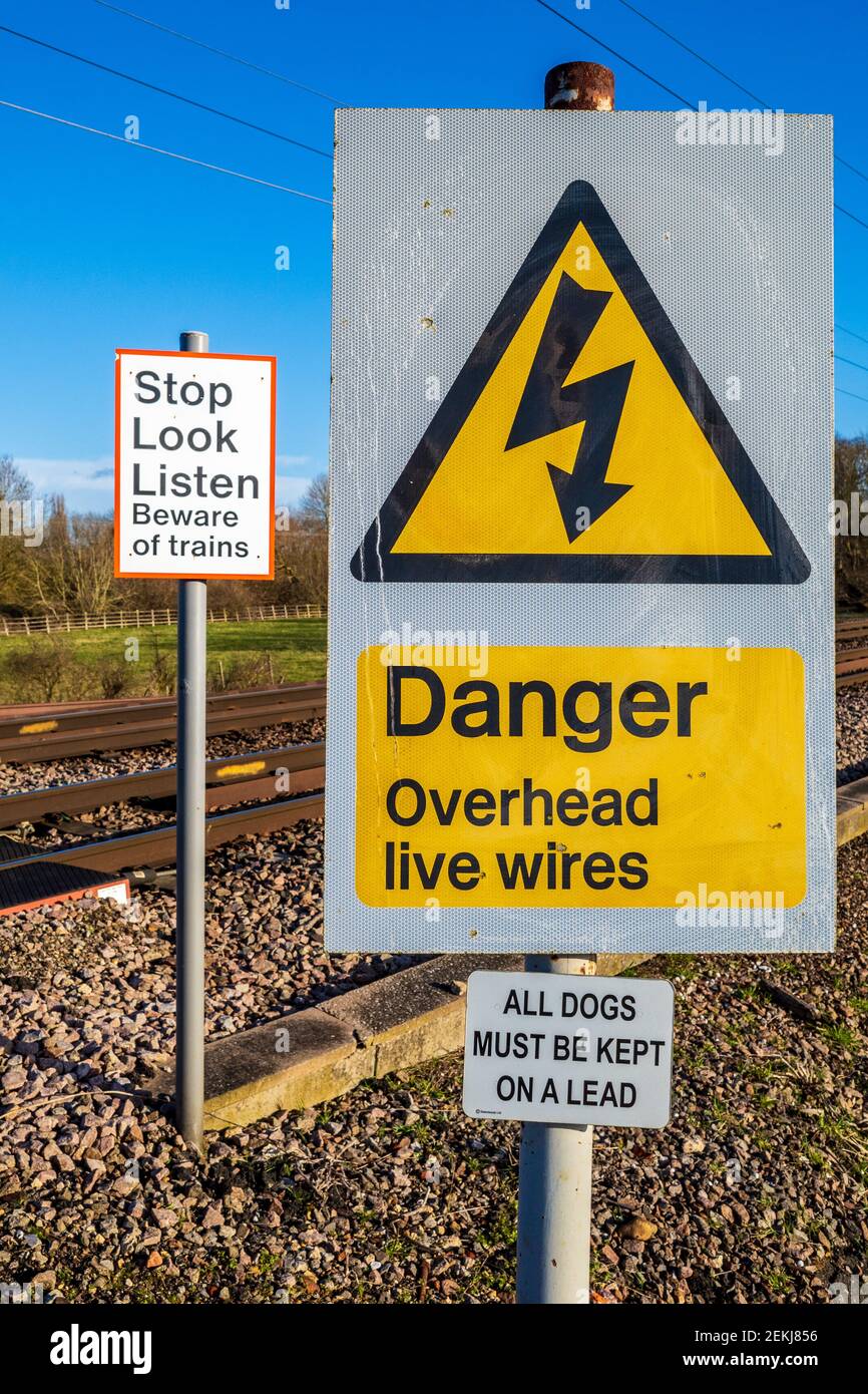 Danger Overhead Live Wires warning sign at an unmanned railway crossing in the UK. Stop Look Listen Beware of Trains warning sign. Crossing Warning. Stock Photo