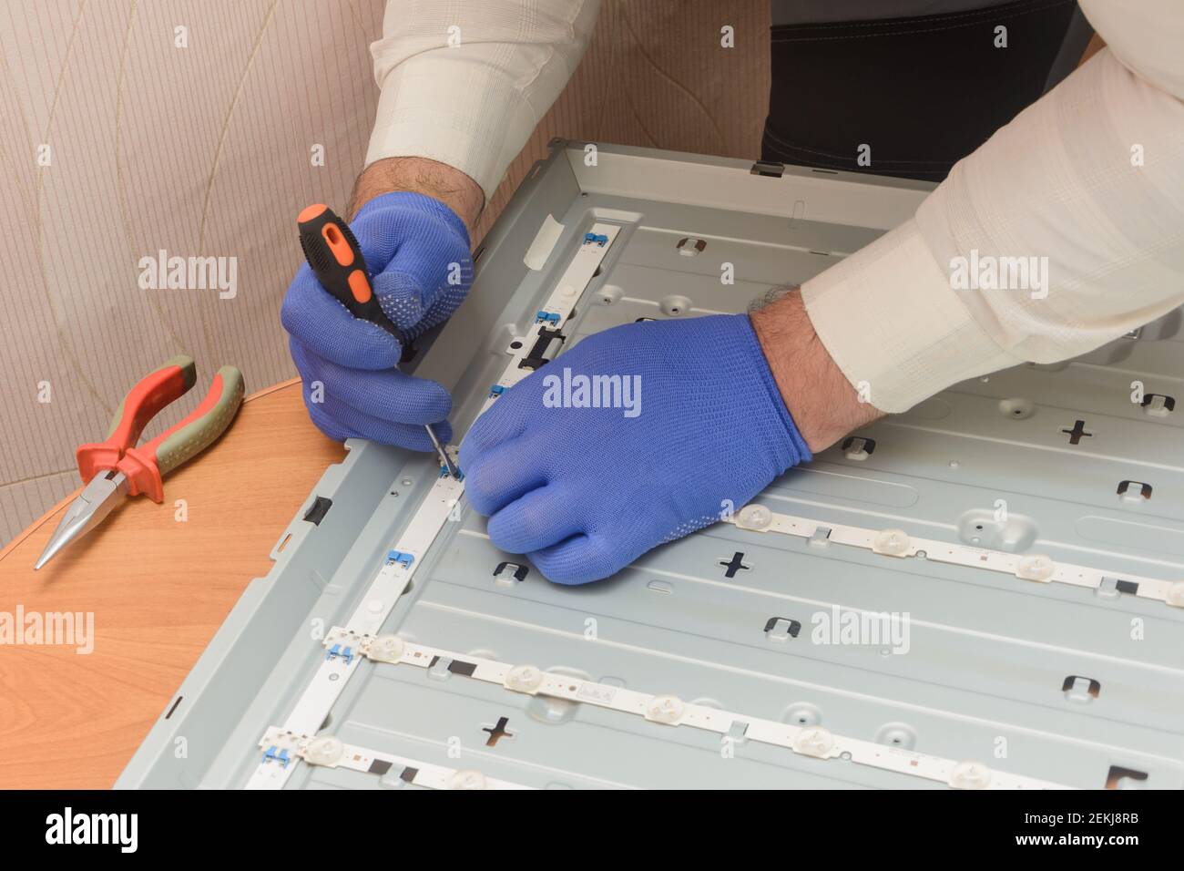 Technician is repairing LCD TV. Hand of master holds dielectric screwdriver, disassembles LED chamber on panel. TV service center. Stock Photo
