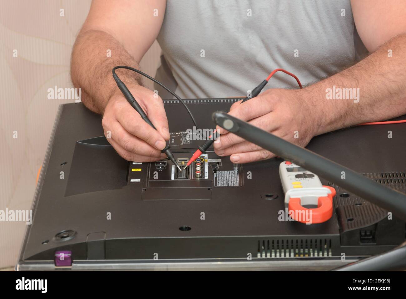 Diagnostics and repair of LCD TV. Engineer takes sample with multimeter on back of large monitor. Stock Photo