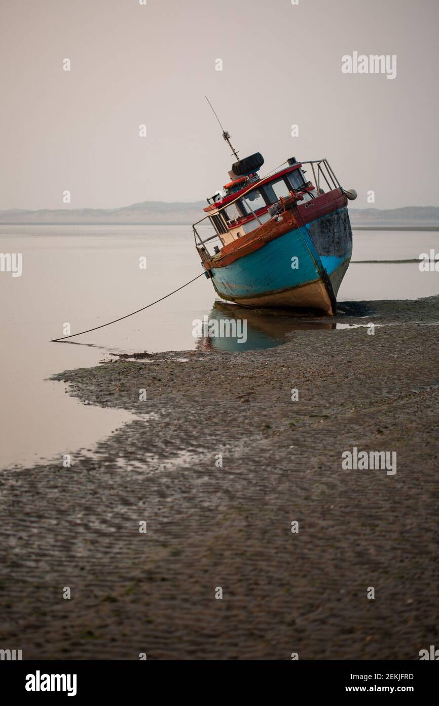 Fishing boat moored on sandy beach at low tide during dusk in winter, Instow, Devon, England Stock Photo