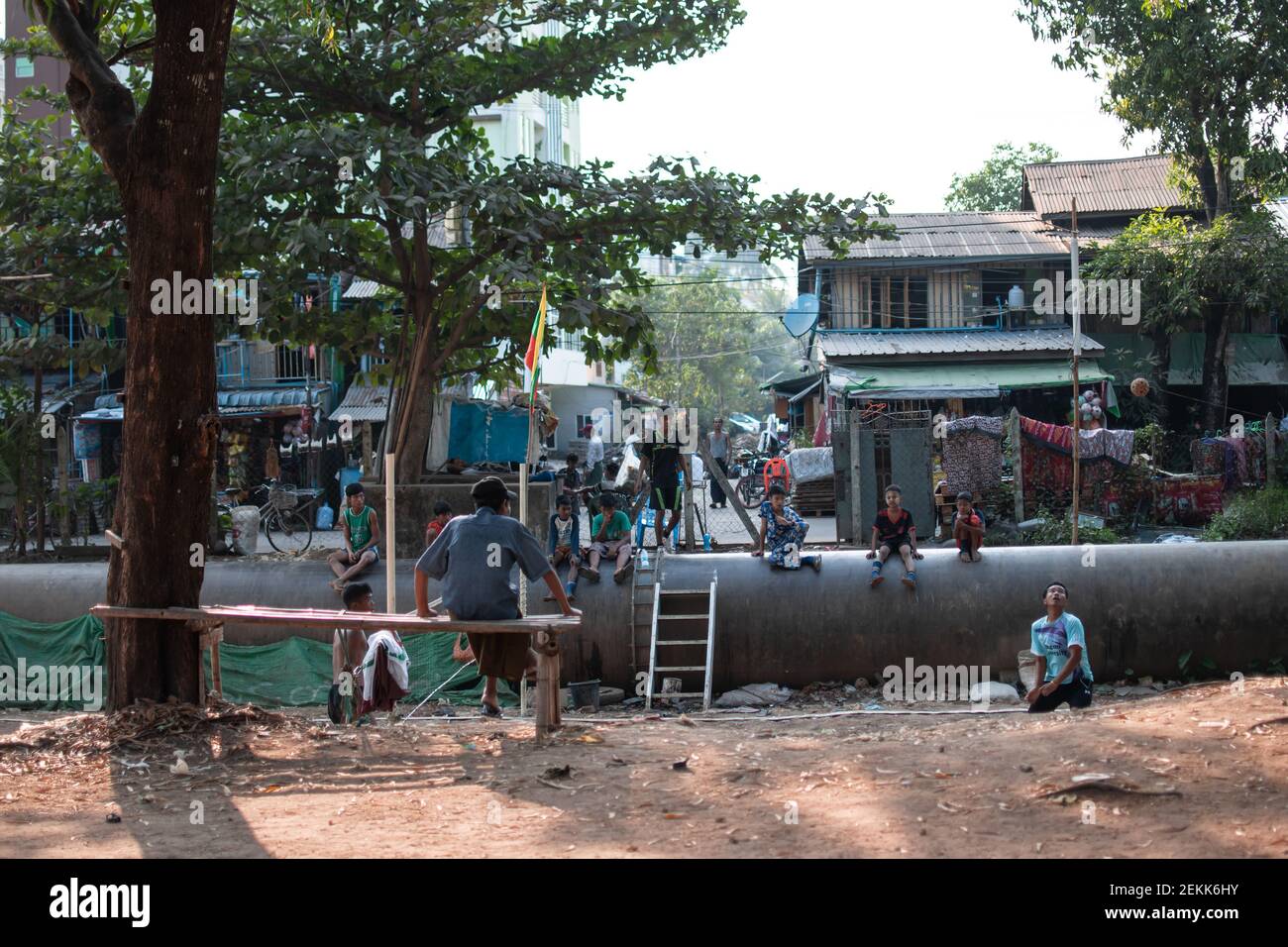 YANGON, MYANMAR - DECEMEBER 31 2019: Local people play traditional chinlone ball with spectators sitting on a pipeline in a village outside Yangon Stock Photo