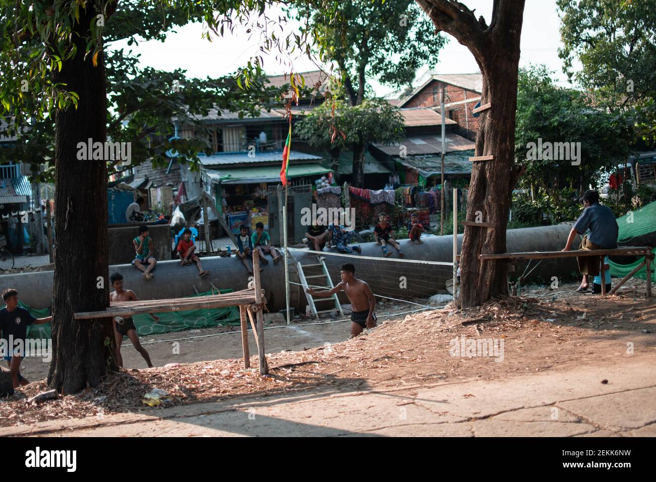 YANGON, MYANMAR - DECEMEBER 31 2019: Local people play traditional chinlone ball with spectators sitting on a pipeline in a village outside Yangon Stock Photo