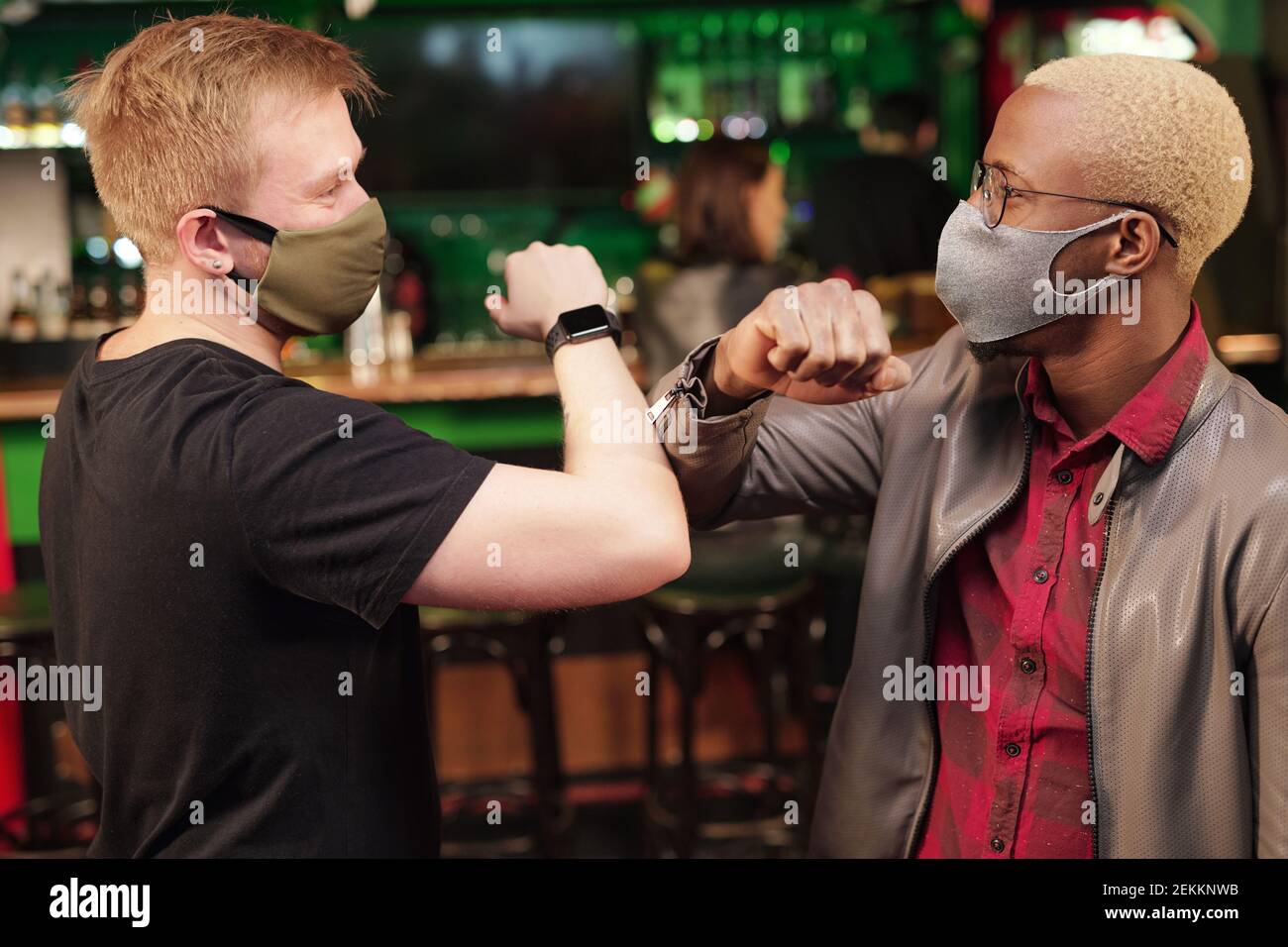 Young men in protective masks greeting each other while standing in the pub during pandemic Stock Photo