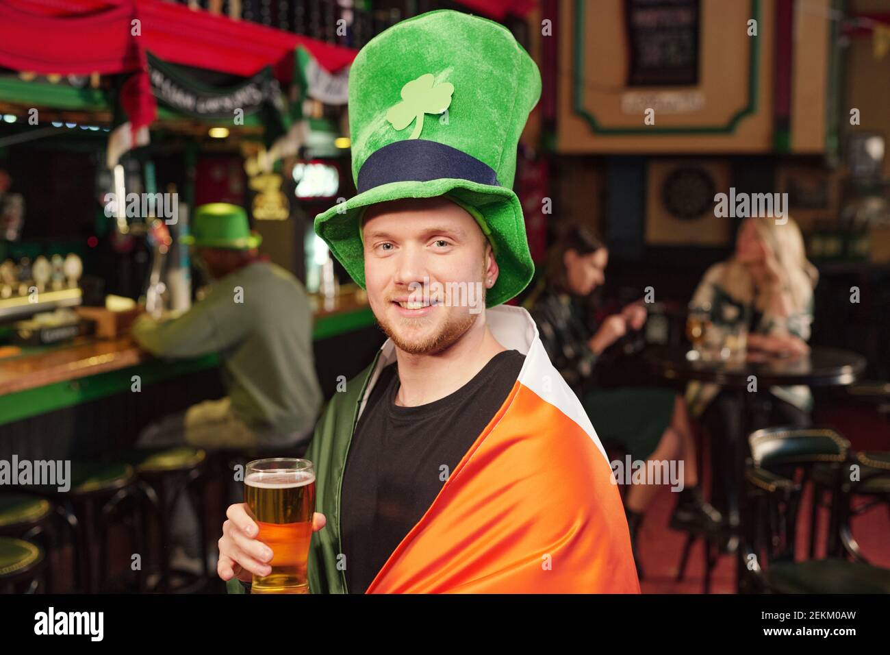 Portrait of happy young man in green hat drinking beer and celebrating Patricks Day in the pub Stock Photo