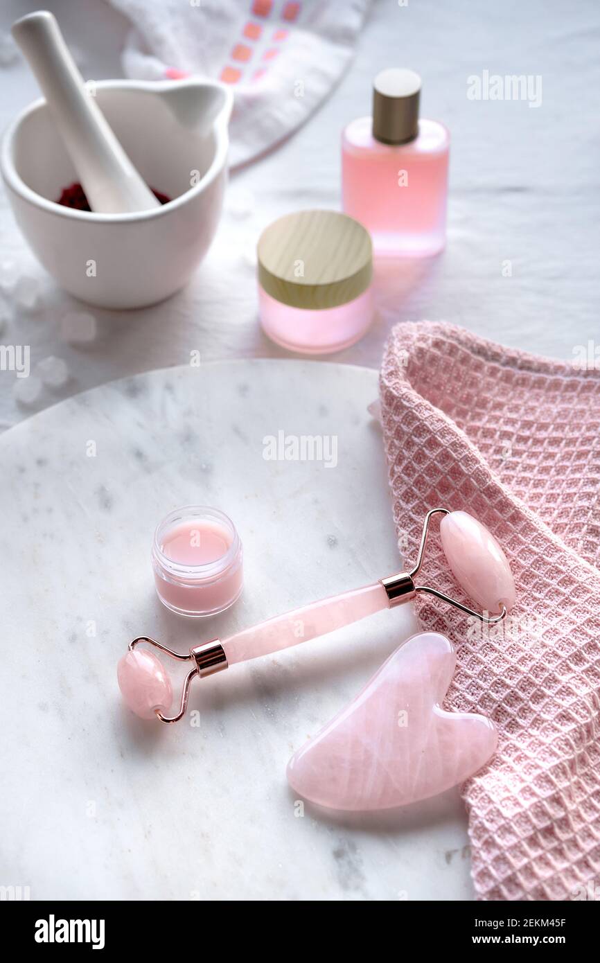 Crystal rose quartz facial roller, Gua sha stone for face massage. Pink  skin care products and oils. Off white marble and textile background,  natural Stock Photo - Alamy
