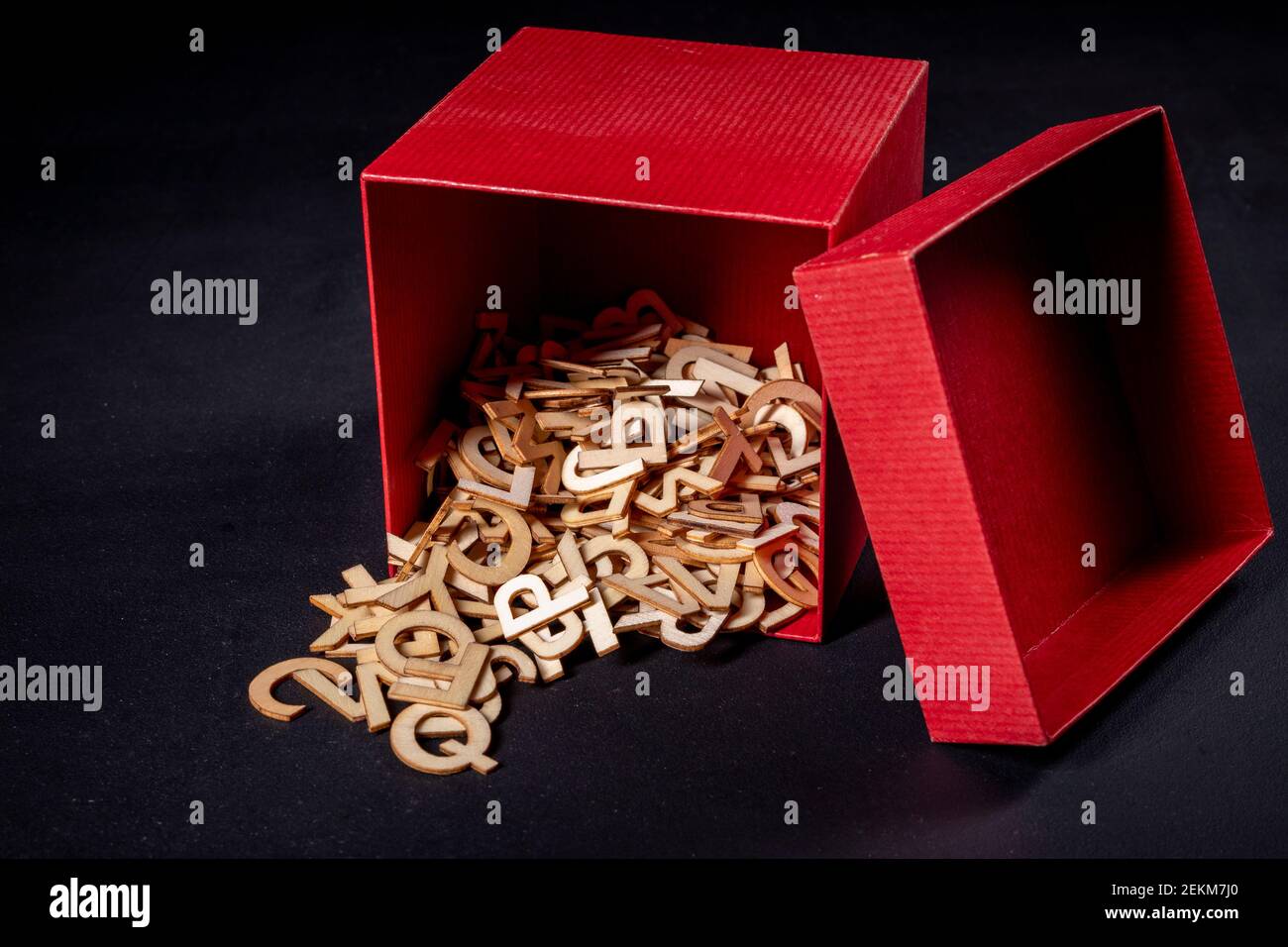 Small wooden letters spilling out of a red box. Outlines of letters with a wood texture used to form words. Dark background. Stock Photo