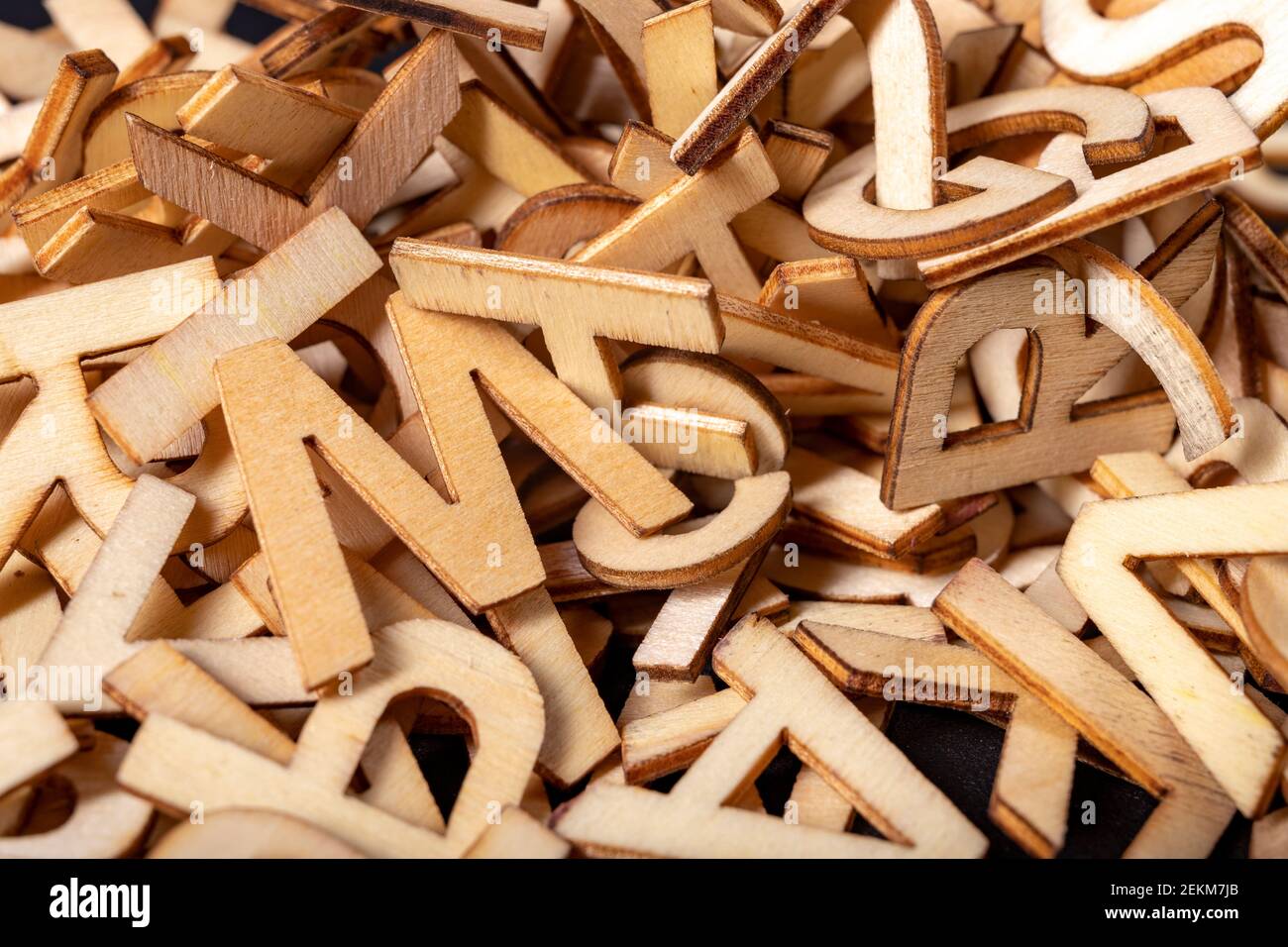 A stack of small wooden letters on a dark table. Letters outlines for arranging inscriptions and words. Dark background. Stock Photo