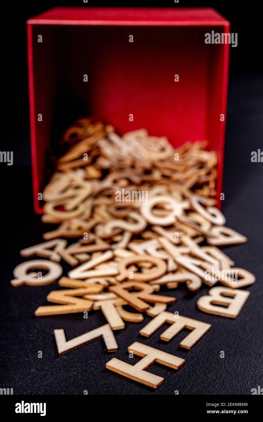 Small wooden letters spilling out of a red box. Outlines of letters with a wood texture used to form words. Dark background. Stock Photo