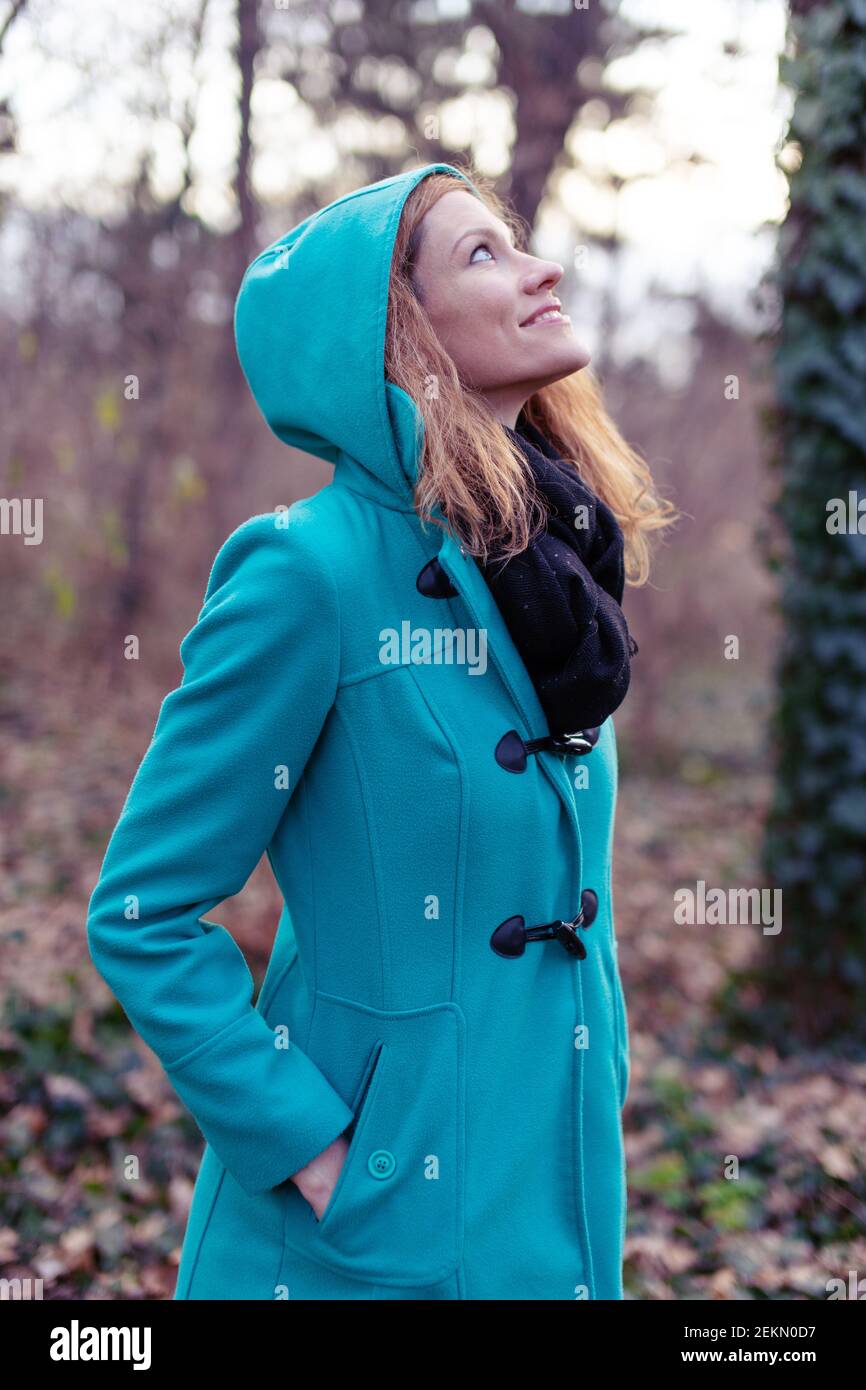 Happy young woman in long coat looking up at cold early spring day Stock Photo